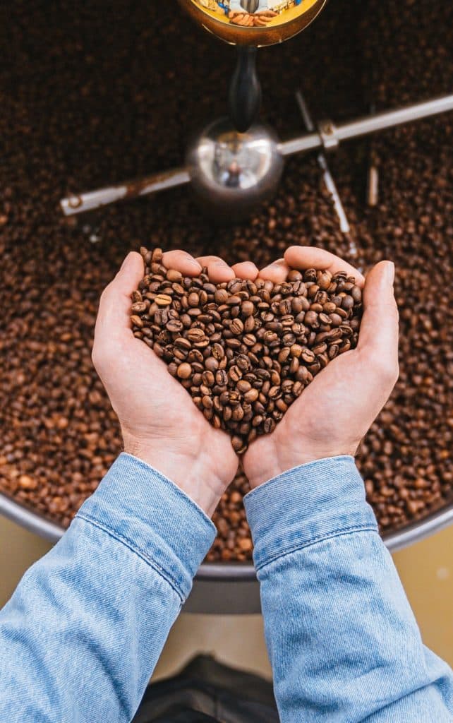 Un torrefacteur tient dans ses mains des grains de café torréfié en forme de coeur