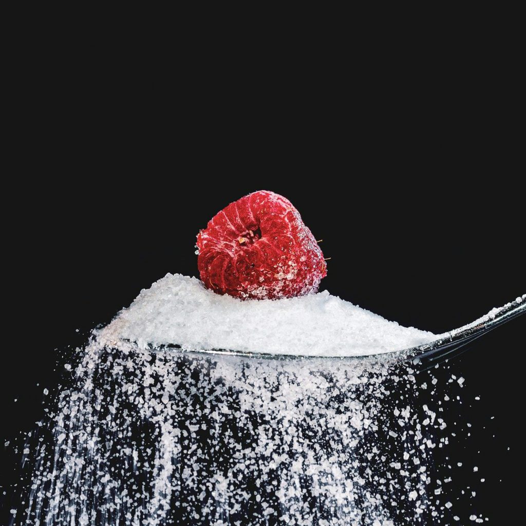 Un framboise est posée sur une cuillère de sucre qui déborde
