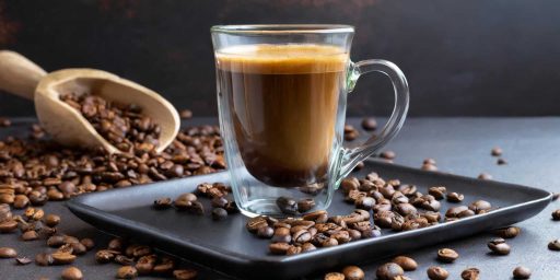 Un café lungo dans une tasse en verre posée sur un plateau de service noir
