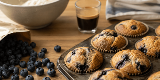Des muffins qui sortent du four, posés sur une table avec un café à côté et quelques ingrédients.