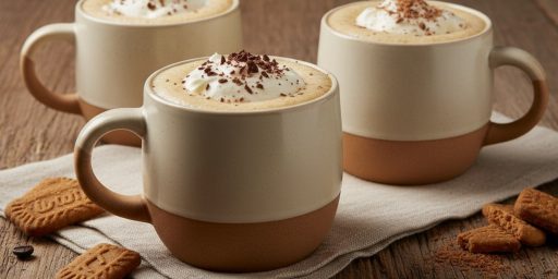 Trois tasses de lait de poule au café, garnies de crème fouettée et de copeaux de chocolat, posées sur une table en bois devant un feu de cheminée.